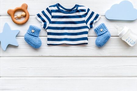 Newborn baby boy set - blue clothes as bodysuit, booties, toys - on white wooden table top-down frame.の写真素材