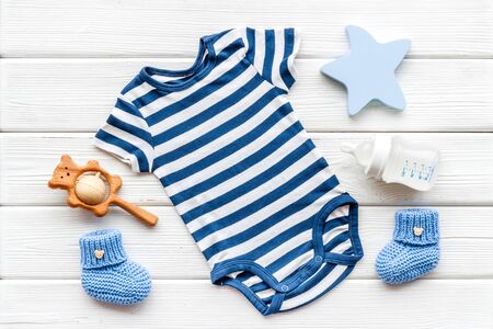 Blue bodysuit for baby boy near children's accessories on white wooden background top-down.の写真素材