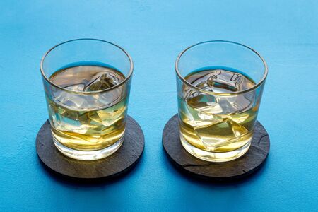 Whiskey with ice. To glasses of strong alcohol drink on blue background.の写真素材