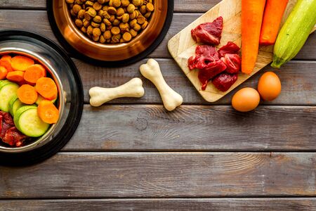 Ingredients of dry feed for dogs - meat, vegetables - near bones on dark wooden background top-down.の写真素材