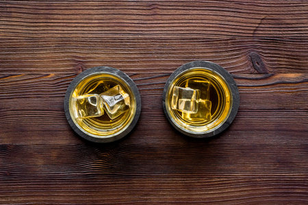 Whiskey with ice. To glasses of strong alcohol drink on dark wooden desk top-down frame copy spaceの写真素材
