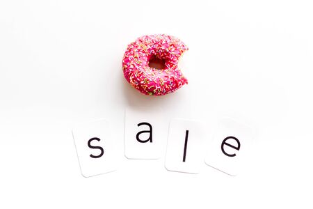 Sales message. Text Sale near bitten donut on white background top-down copy spaceの写真素材