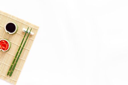 Table served for eating sushi. Chopsticks, bowls with ginger and sause, mat on white background top-down copy spaceの写真素材