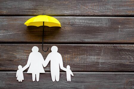 Health insurance concept. Family cutout under umbrella on dark wooden background top-down copy spaceの写真素材