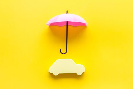Car insurance. Automobile toy under umbrella on yellow background top-down copy spaceの写真素材