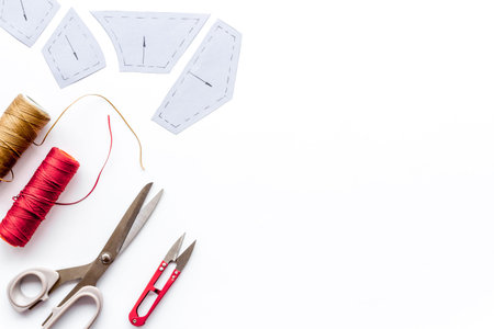 Clothes designer work desk. Pattern, scissors, thread on white background top-down