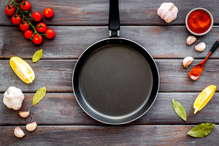 Cooking mock up. Frying pan among spices and vegetables on dark wooden background.の写真素材