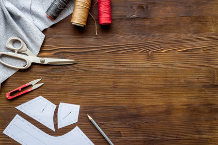 Sewing wokrshop. Textile, pattern, scissors, thread on dark wooden background top-down.