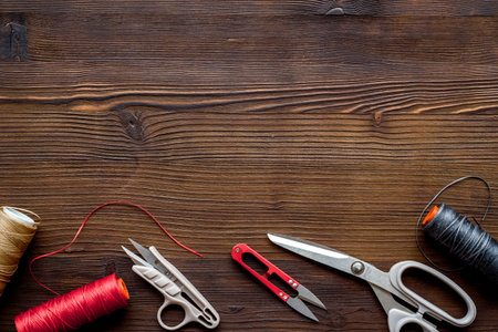 Tailor's work desk. Thread and sciccors on dark wooden background top-down.
