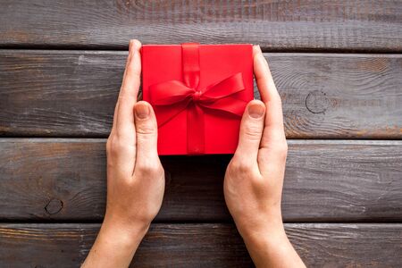 Give a gift on Valentine's Day. Women hand hold beautiful red present box on dark wooden background top-down.の写真素材