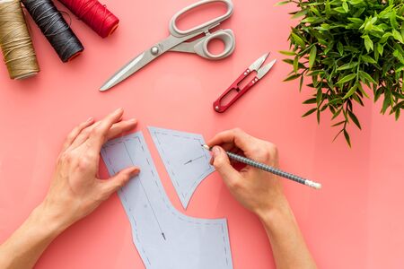Tailor working. Women hands drawing patterns for clothes on pink background top-down.の写真素材