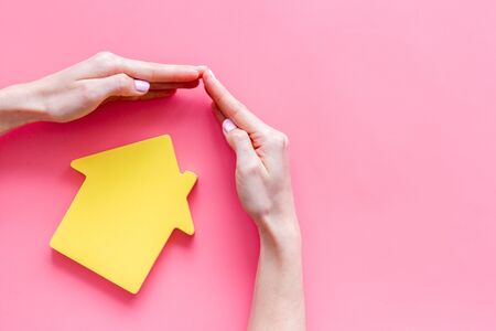 Property insurance concept. Hand defends house cutout on pink backgound top view.の写真素材