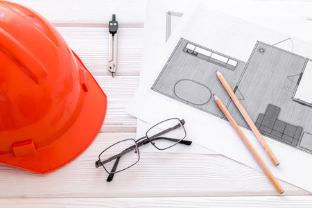 Builder helmet and blueprints on white wooden background.