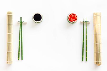 Oriental table set up. Chopsticks, ginger, soy sauce, bamboo mat on white background top-down.の写真素材