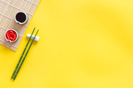 Oriental table set up. Chopsticks, ginger, soy sauce, bamboo mat on yellow background top-down frame copy spaceの写真素材