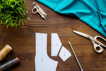 Clothes designer work desk. Pattern, scissors, thread on dark wooden background top-down.