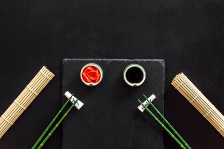Table served for sushi. Chopsticks, small bowls with ginger and sause, mat on black background top-down.の写真素材