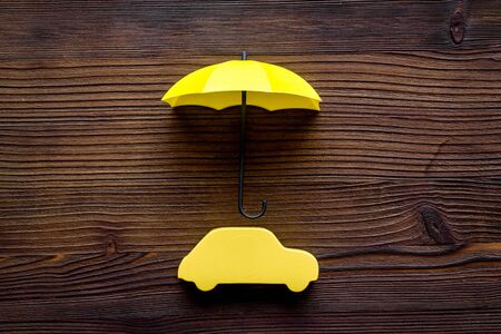 Car protection concept. Automobile cutout defended by umbrella on dark wooden background top-down copy spaceの写真素材