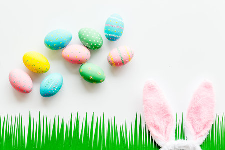 Easter concept. Eggs, Bunnys ears and grass on white background top-down copy space