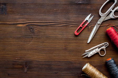 Tailors work desk. Thread and sciccors on dark wooden background top-down copy space