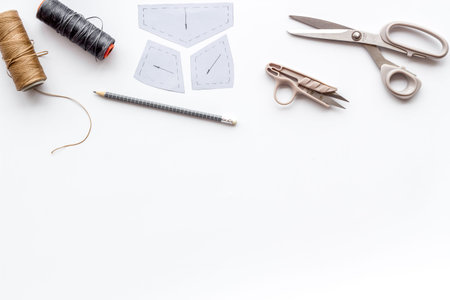 Clothes designer work desk. Pattern, scissors, thread on white background top-down copy space