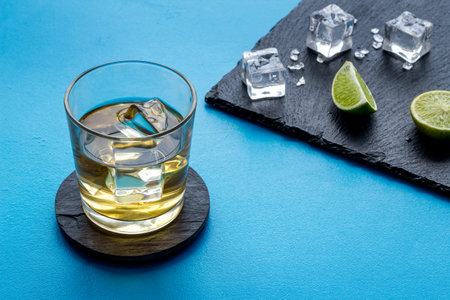 Whiskey near ice cubes on blue background copy space