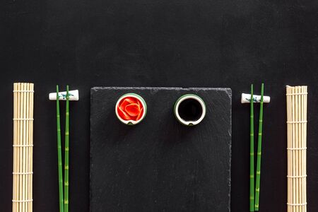 Table served for eating sushi. Chopsticks, small bowls with ginger and sause, mat on black background top-down copy spaceの写真素材