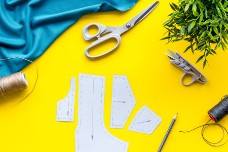 Clothes designer work desk. Pattern, scissors, thread, textile on yellow background top-down.