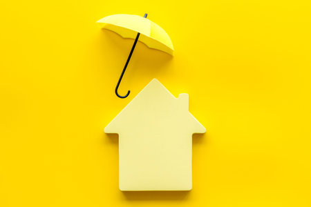 House protection concept. Toy house defended by umbrella on yellow background top view copy spaceの写真素材