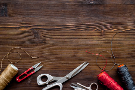 Tailor's work desk. Thread and sciccors on dark wooden background top-down.