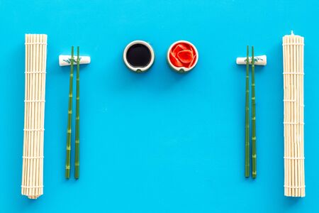 Oriental table set up. Chopsticks, ginger, soy sause, bamboo mat on blue background top-down frame copy spaceの写真素材