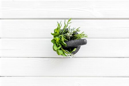 Herbs in ceramic mortar with pestle on white wooden backgroud top-down.の写真素材