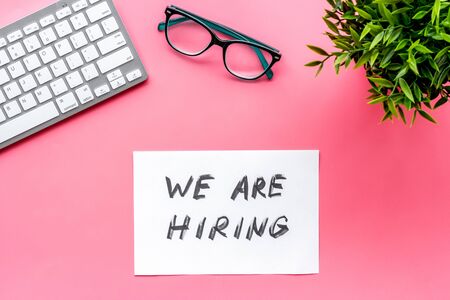 We are hiring. Text on pink office desk top-down.の写真素材