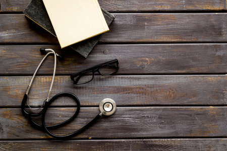 Medical books near stethoscope on dark wooden background top-down copy space