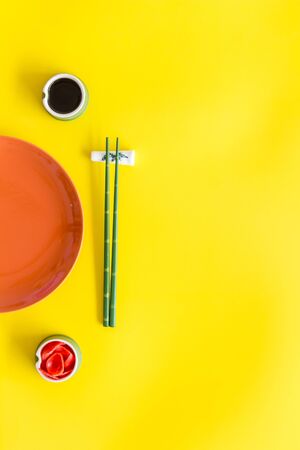 Tableware for sushi and rolls. Plate, chopsticks, small bowls with ginger and sause on yellow background top-down copy spaceの写真素材