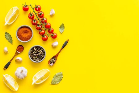 Cooking background with spices and vegetables - pepper, garlic, cherry tomatoes - on yellow desk top-down.の写真素材