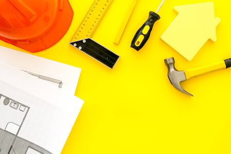 Construction concept. Helmet, tools on work desk, house cutout on yellow background top-down frame.の写真素材