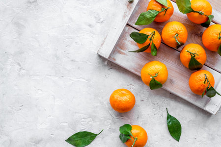 Tangerines with leaves on tray - as fruit harvest - on grey background top-down.