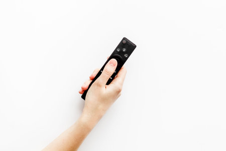 Watch TV concept. TV remote in hand on white background top-down copy space