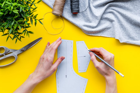 Tailor working. Women hands drawing patterns for clothes on yellow background top-down