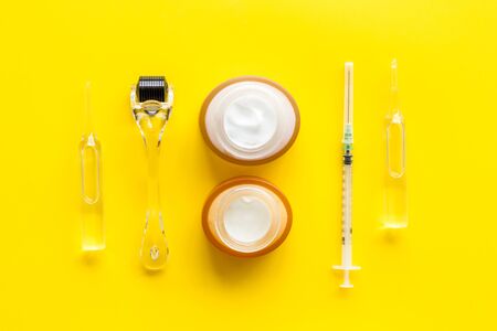 Dermatologist work desk with tools. Dermaroller, syringe, ampoule on yellow background top-down.の写真素材