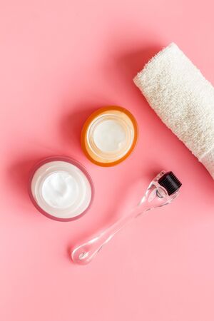 Cosmetology and skin care concept. Dermaroller, creams on pink background top-down flat layの写真素材