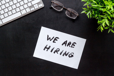 We are hiring. Text on black office desk top-down.