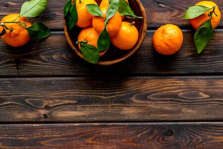 Ripe tangerines on dark wooden table. Citruses with green leaves in bowl top-down copy spaceの写真素材