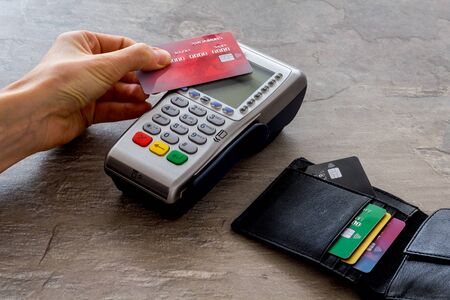 Contactless payment, paypass. Hand hold bank card near terminal on grey stone background.