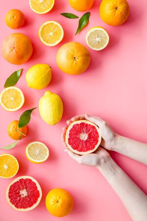 Fresh citrus background with fruit in hands. Oranges, grapefruits, leaves on pink background top-down.の写真素材