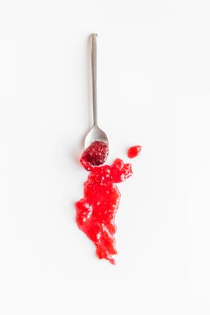 Fruit jam. Red dessert smashed by spoon on white deskの写真素材