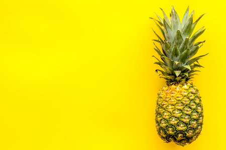 Pineapple - whole fruit - on bright yellow background top-down.