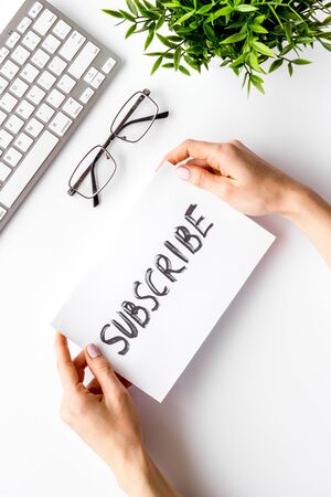 Subscribe. Advertisement in hand on white office desk top-down.の写真素材