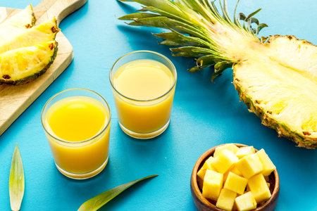 Pineapple juice in glass near sliced fruit on blue background.